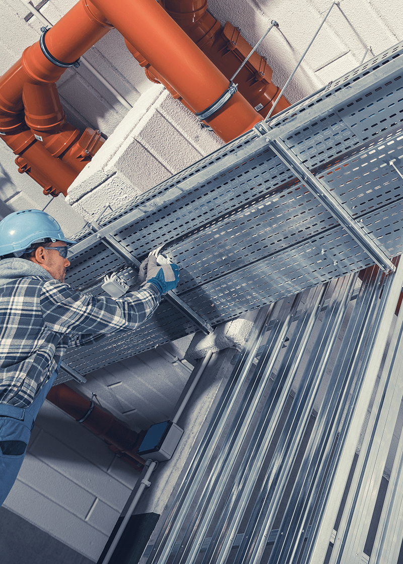 Low-voltage electrician installing cable ladders in a commercial setting, with orange piping and structured cabling visible, emphasizing network installation expertise.