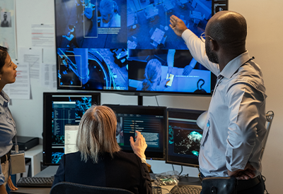 Team of professionals in a control room analyzing data on multiple screens, discussing fiber connectivity solutions for high-security government projects.
