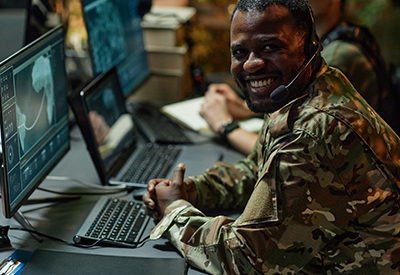 Military personnel in camouflage uniform working at a computer station, engaged in mission-critical communications and fiber connectivity for government projects.