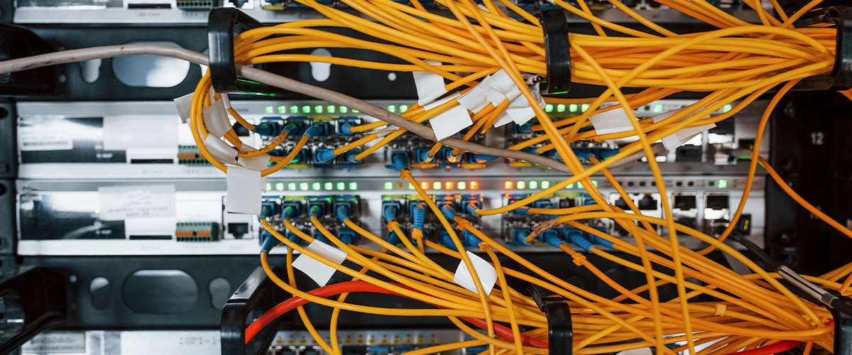 Network cabling setup with yellow fiber optic cables and illuminated switches, illustrating advanced infrastructure for data centers by Universal Fiber Optics.