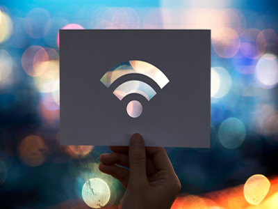 Hand holding a paper with a cutout of a Wi-Fi symbol, set against a blurred cityscape background, representing wireless network installation services for businesses.
