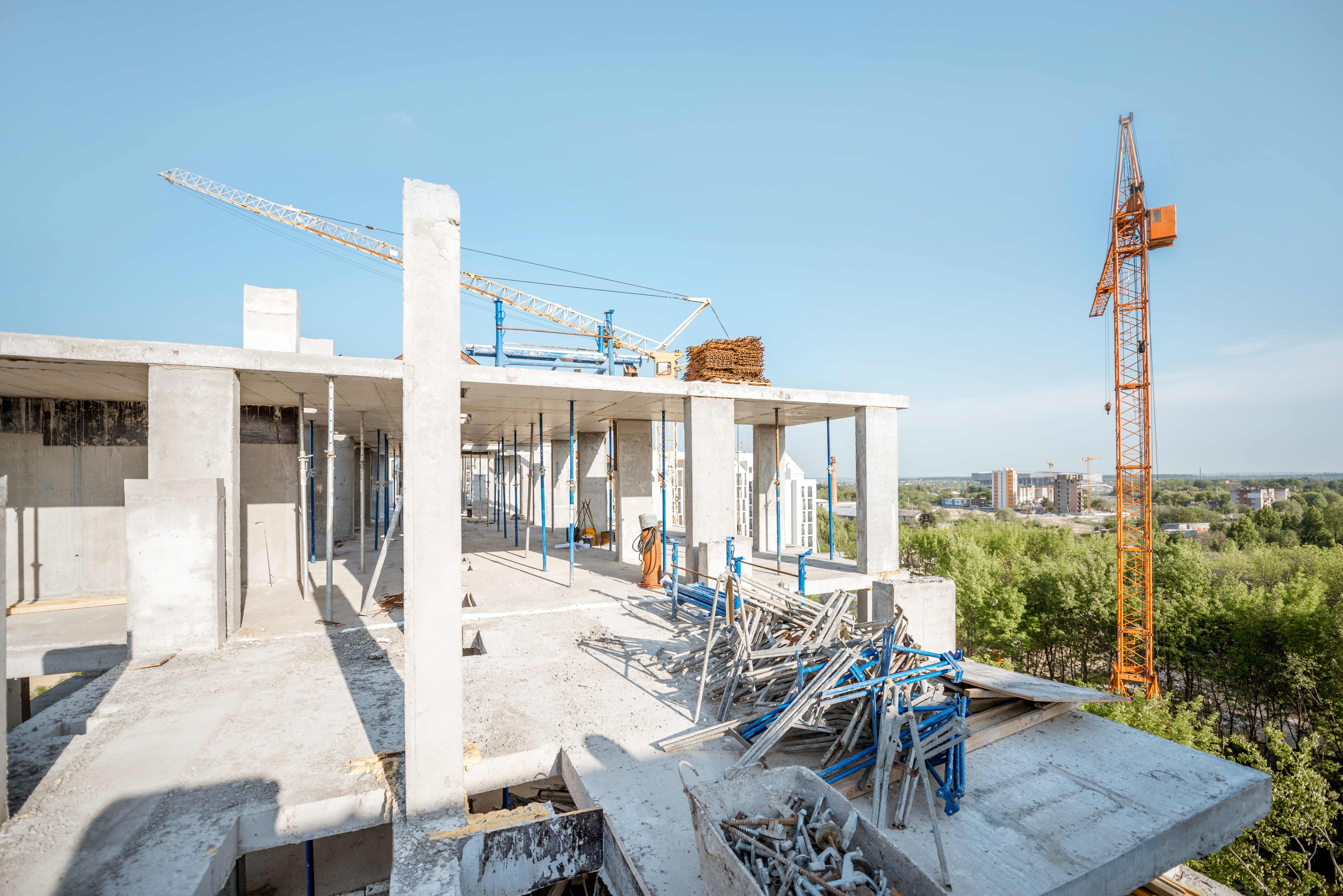 Construction site of a new building featuring exposed concrete structures, scaffolding, and a tower crane against a clear sky, illustrating advanced infrastructure for network cabling installation.