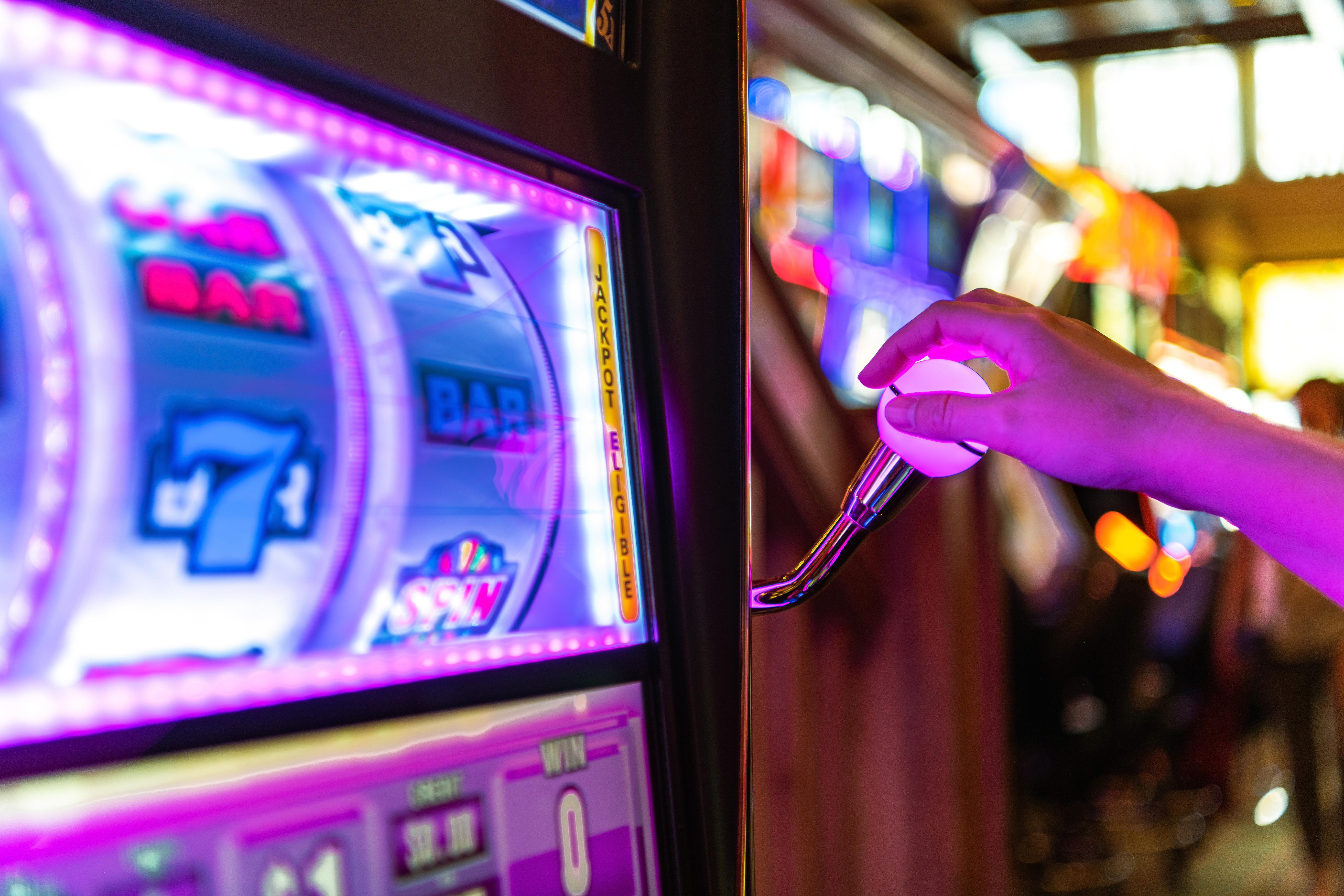 Hand reaching for the lever of a brightly lit slot machine in a casino, showcasing vibrant colors and gaming excitement, relevant to network cabling services for hospitality and entertainment industries.