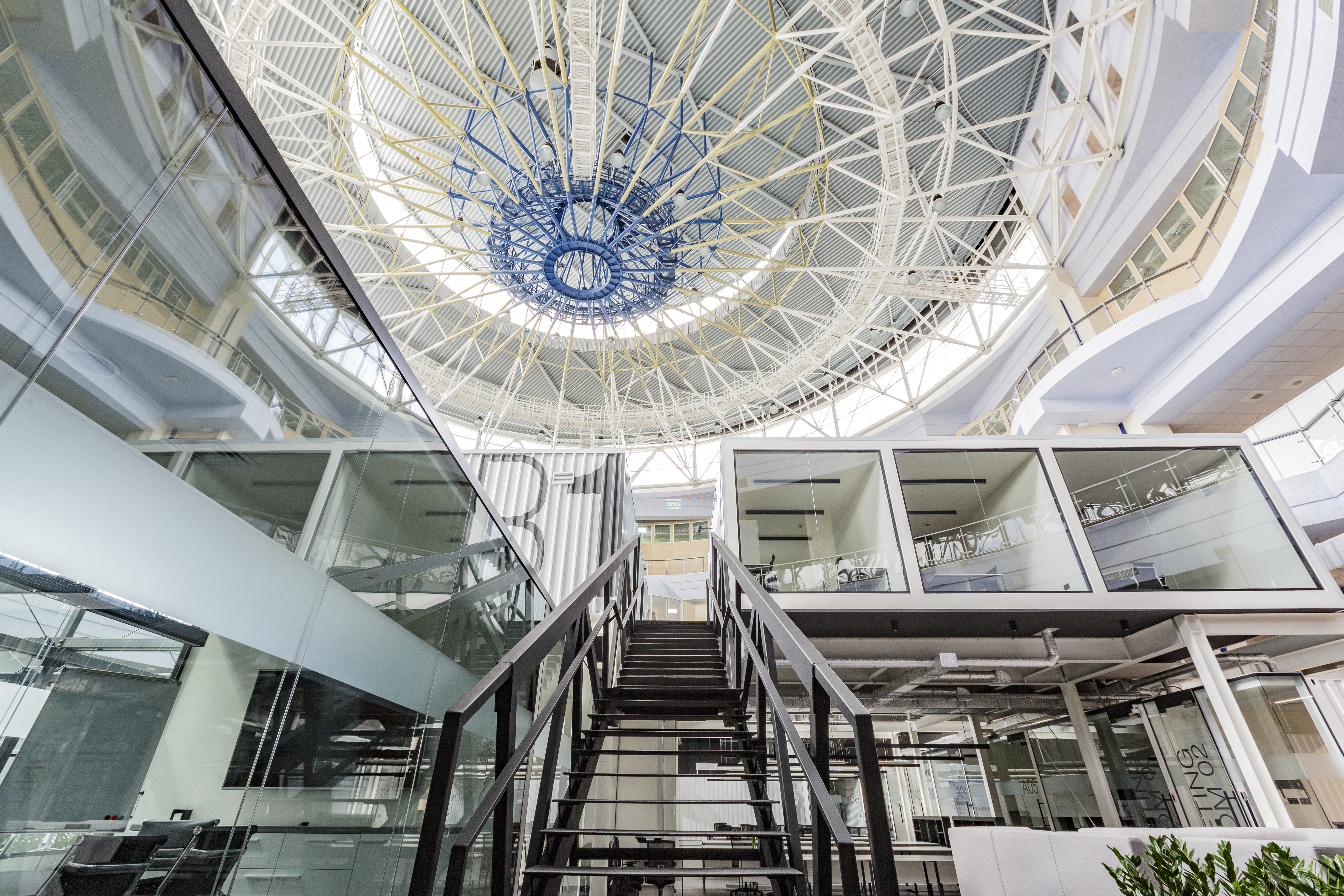 Modern office interior with glass walls, metal staircase, and a high, intricately designed ceiling, reflecting advanced infrastructure for network cabling services.