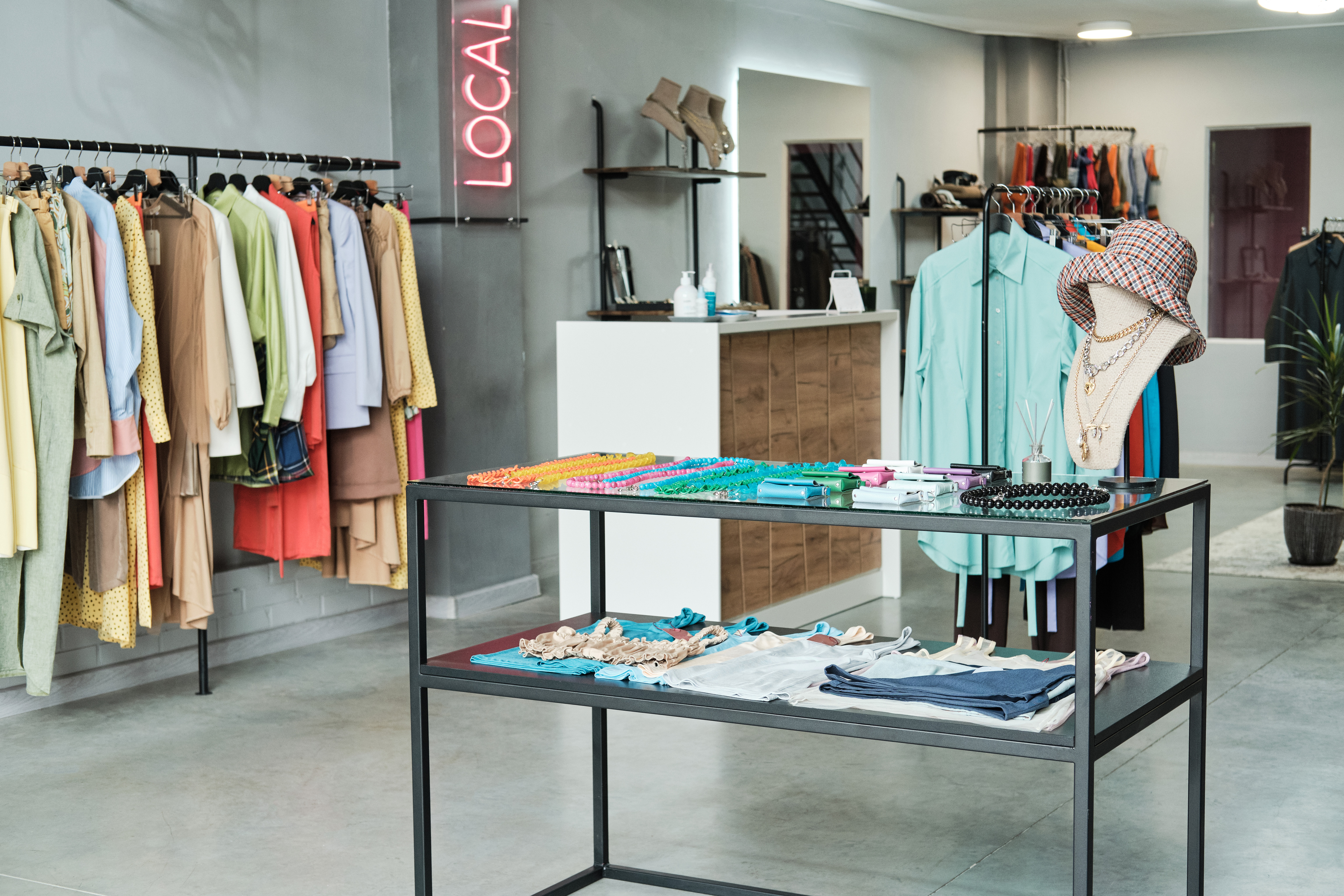 Colorful clothing display in a retail store with accessories on a table, featuring a neon "LOCAL" sign, emphasizing vibrant fashion and local shopping.