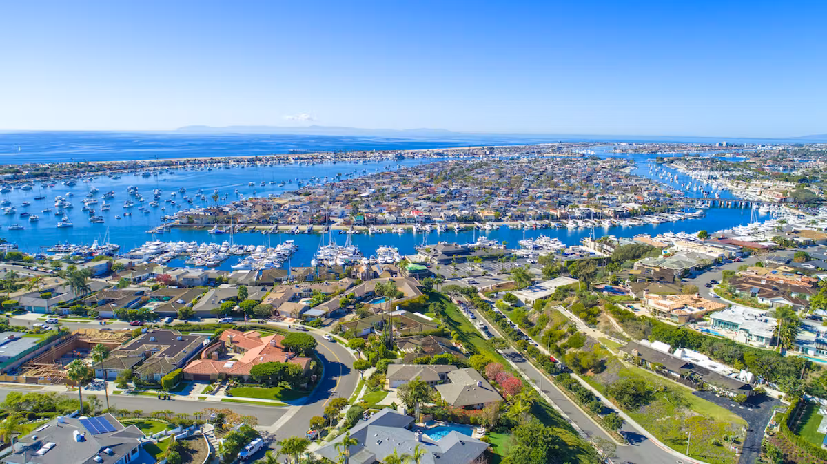 Aerial view of Orange County coastline featuring residential areas, marinas with boats, and clear blue skies, highlighting the region's vibrant landscape relevant to low voltage services offered by Universal Fiber Optics.